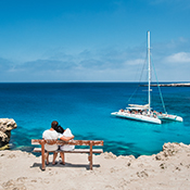 Couple sitting on a bench looking out at ocean and boat in Cyprus